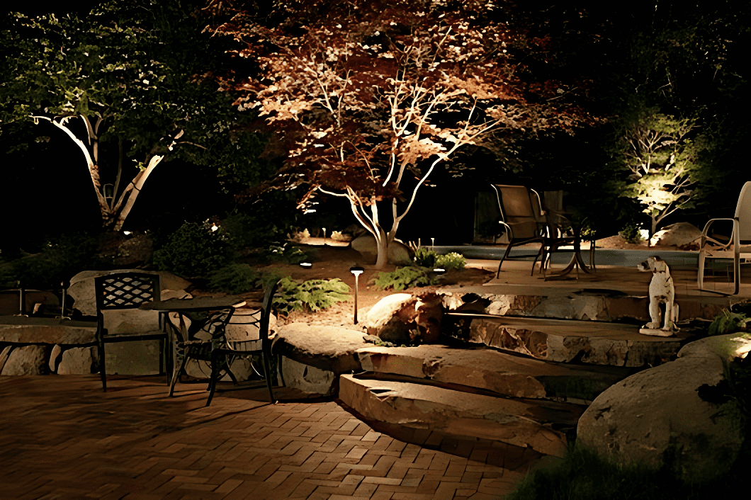 A dimly lit backyard patio with stone steps, chairs, trees, and a dog statue at night.