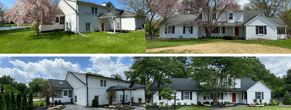 Four white houses with black roofs and red doors situated in grassy areas with trees.