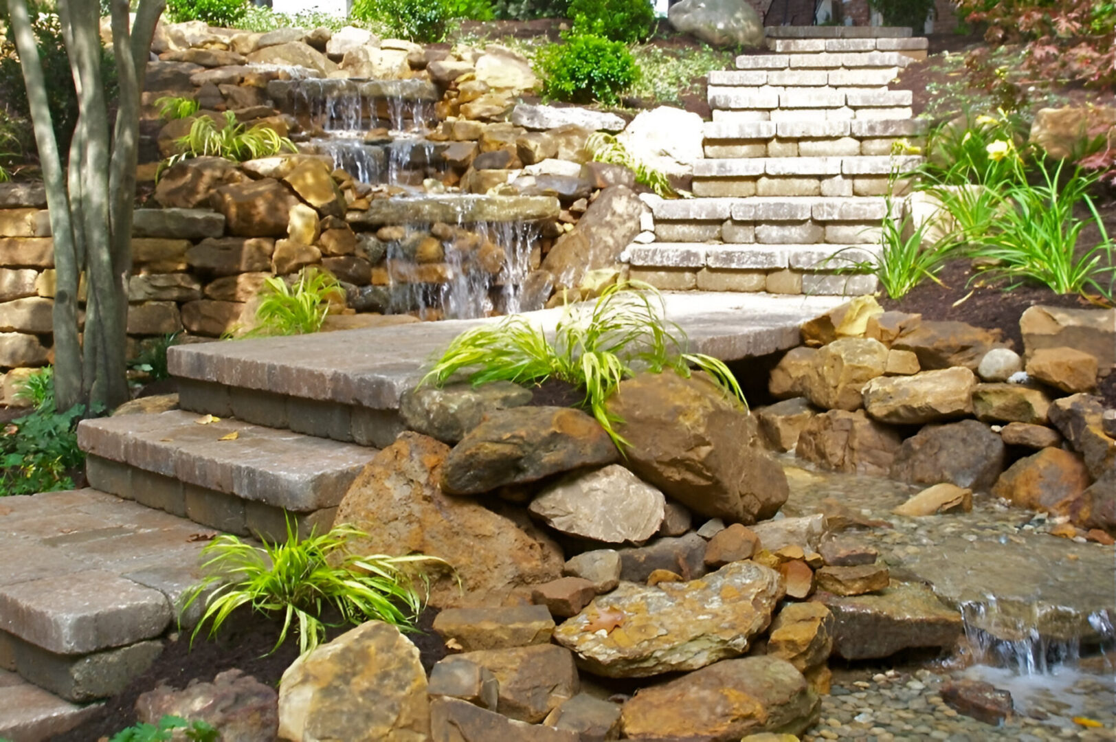 Stone stairway with a cascading waterfall feature and surrounding rocks and greenery.