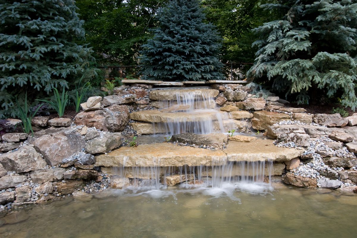 Garden waterfall with stones and evergreen trees.