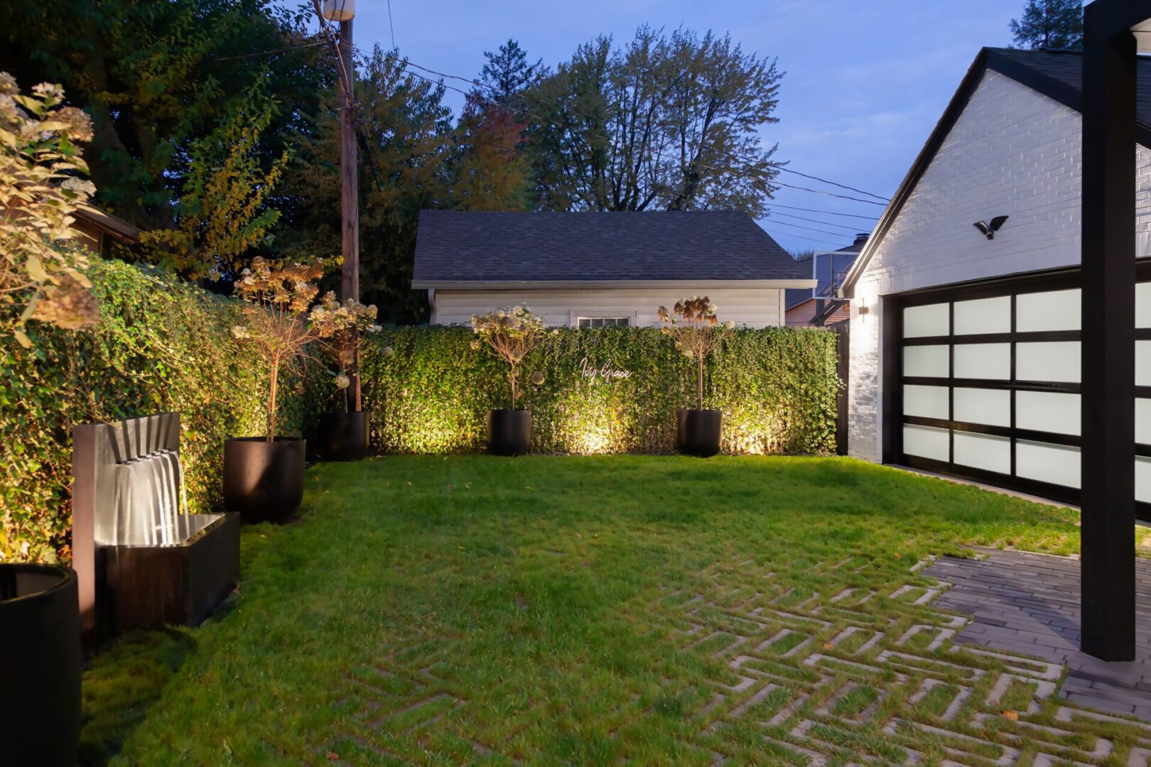 Illuminated backyard with plants and modern garage.